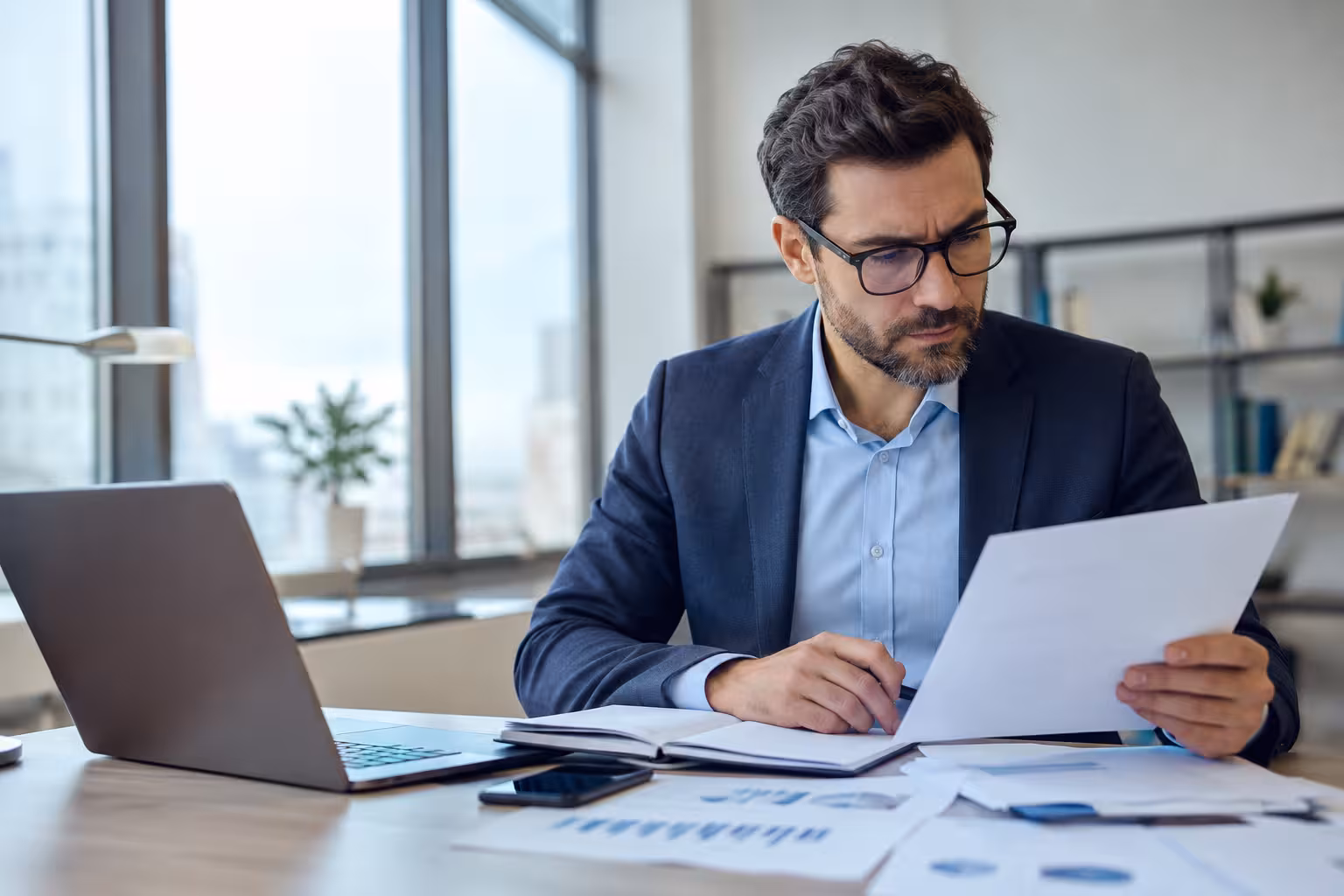 Professional reviewing financial statements and supporting records beside a laptop